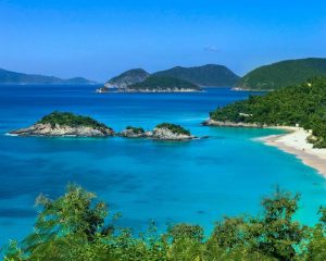Trunk Bay in St John, a remote beach with white sand with bright blue water edged by greenery.