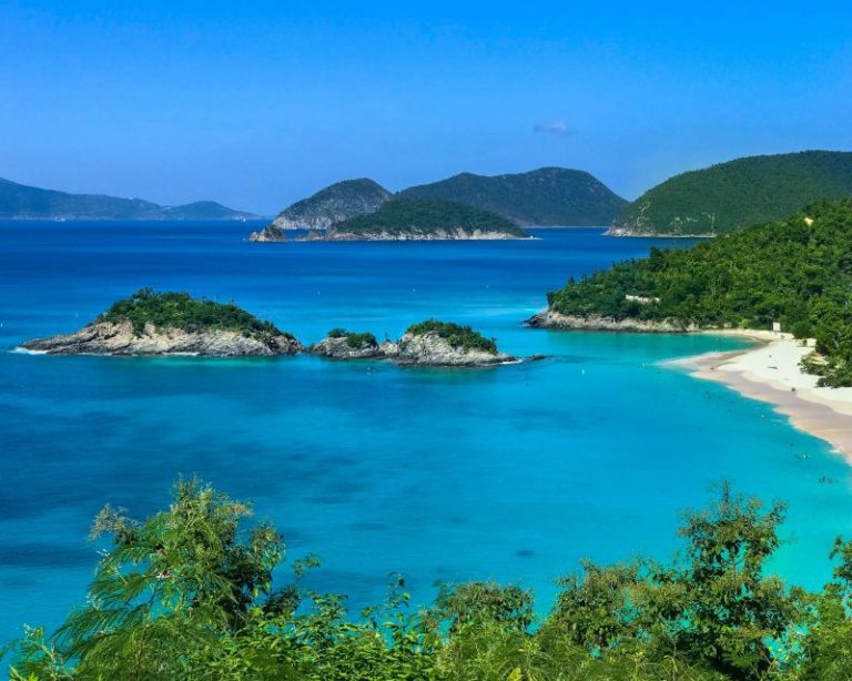 Trunk Bay in St John, a remote beach with white sand with bright blue water edged by greenery.