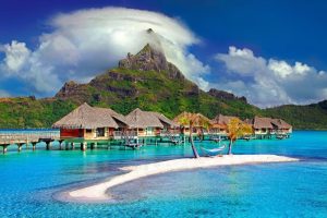 Beautiful, over teh water bungalows in Bora Nora. There is blue water in teh foreground and beautiful green mountains in the back ground.