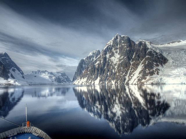 An Antarctica cruise.  You can see the bow of the ship in the foreground, and imposing black and white mountains in the background past still water (you can see the reflections of the mountains in the water.)